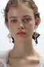 Model wearing Vesper Star Drops mixed-metal statement earrings with a soft white blouse and black ribbon detail